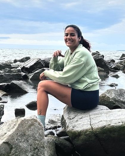 Mahsa Dehghani Rad sitting on shoreline rocks by a lake